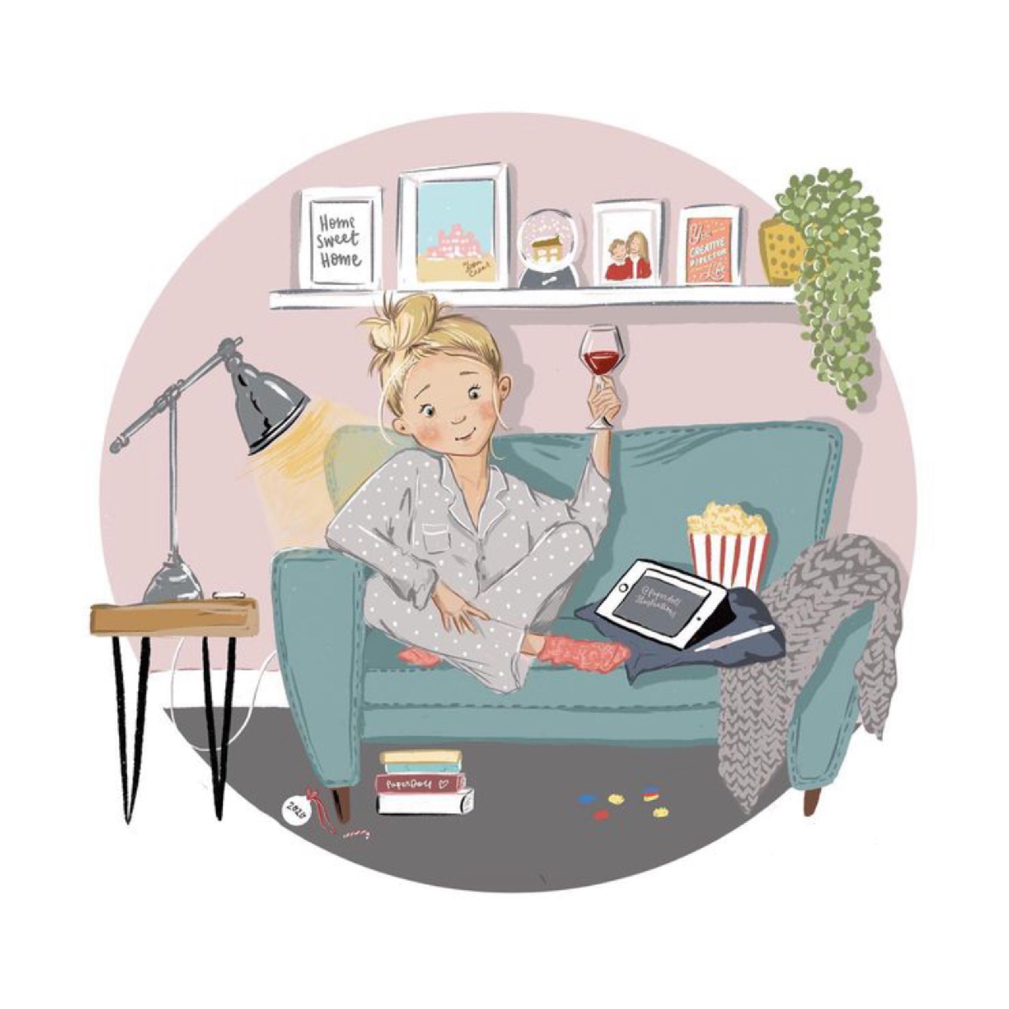 Blonde white woman in blue pyjamas hold a glass of red wine sitting on a comfy sofa with po-corn and an ipad resting next to her